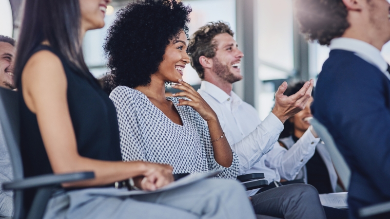 Employees smiling and clapping during a workplace event, showing engagement and positive morale