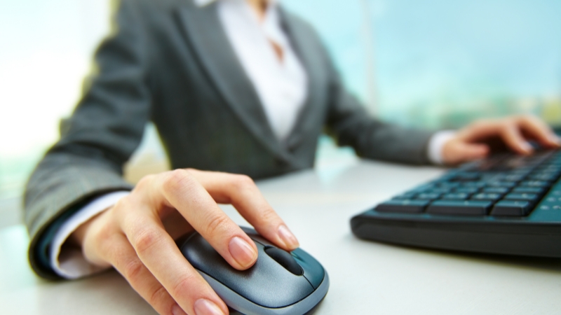 A person in a business suit uses a computer mouse and keyboard at a desk