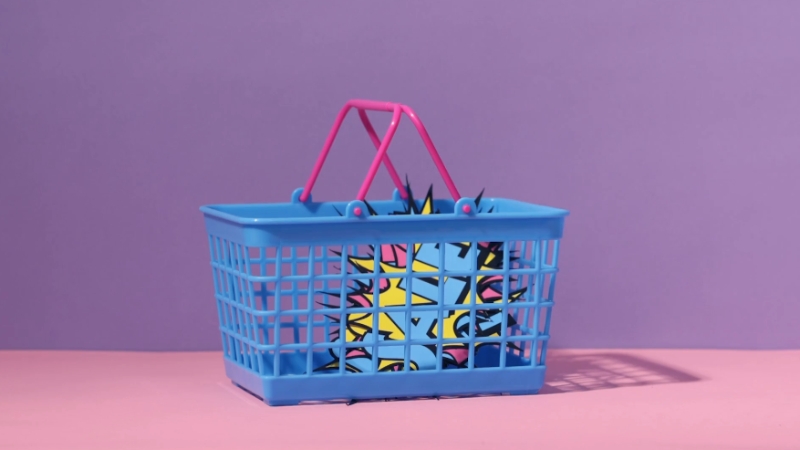 A blue shopping basket with pink handles holds a colorful graphic design against a purple background