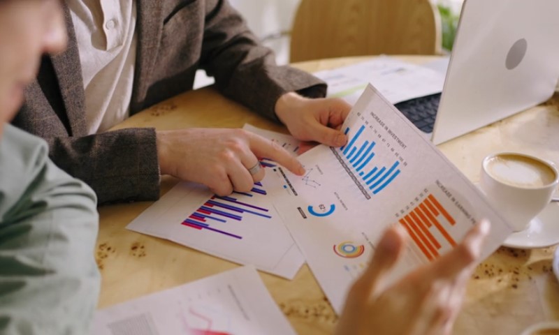 Two individuals analyze graphs printed on papers, engaged in discussion about the data presented