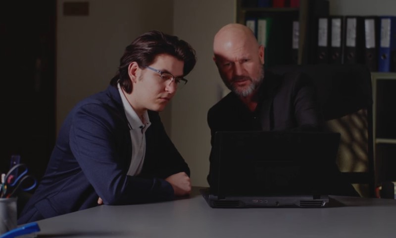 Two men in suits are collaborating while looking at a laptop computer