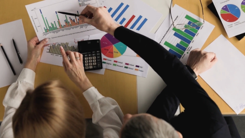 Two people analyzing business charts and graphs to identify the key factors driving their company’s economic engine
