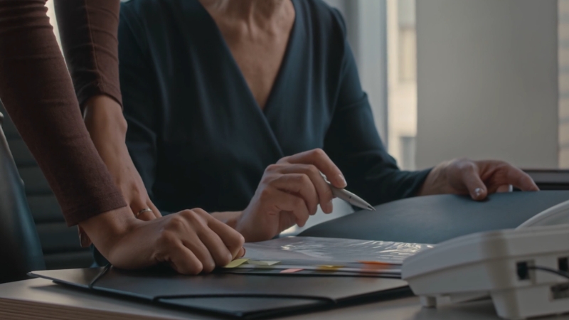 Two colleagues discuss documents at a desk while reviewing market conduct and firm strategies