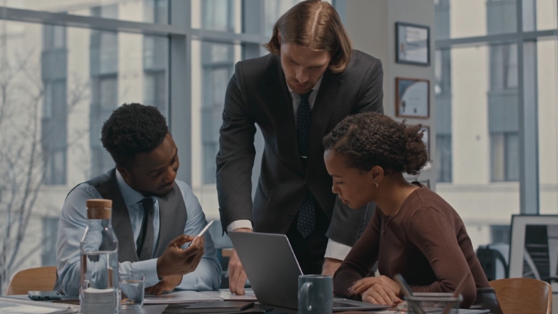 Business professionals collaborate at a desk, reviewing data on a laptop to discuss the SCP model in the digital economy