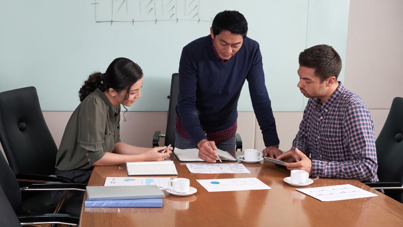 Three professionals review charts and documents in a meeting room while planning a Product Matrix Strategy