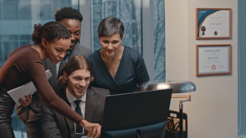 A group of business professionals reviews data on a computer while discussing strategic insights from the SCP model
