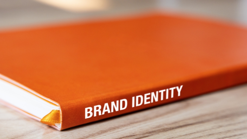 An orange hardcover book with the title “Brand Identity” on the spine