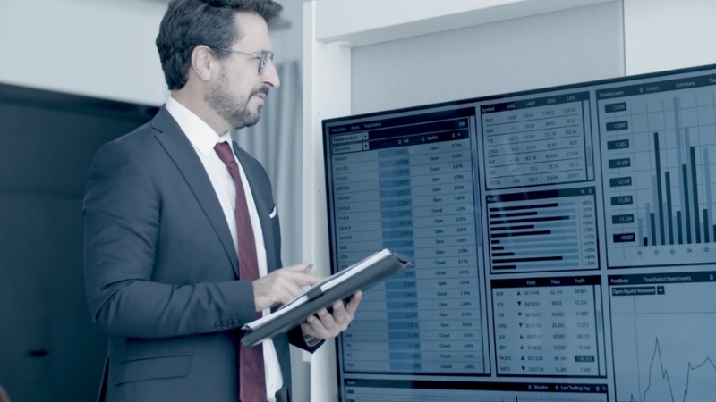 A businessman reviewing financial charts and data on a large screen to assess the company’s economic engine performance