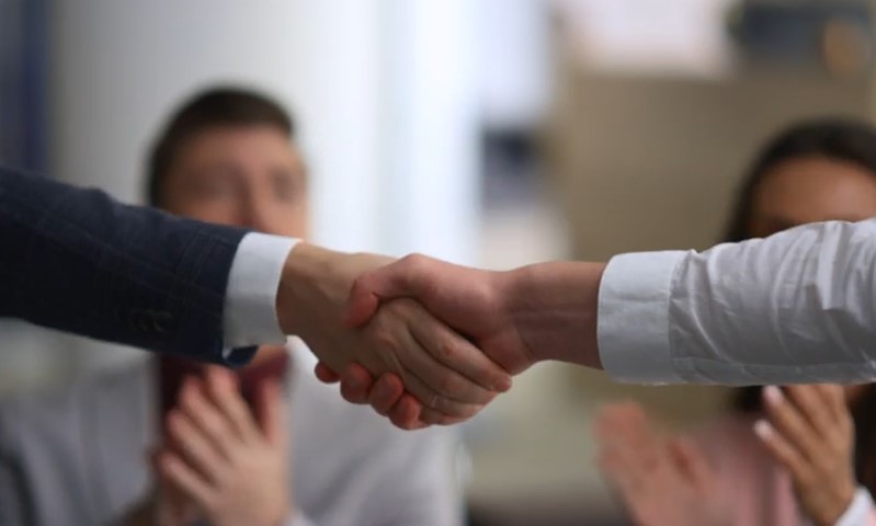 Two people shaking hands in front of a group, symbolizing agreement or partnership