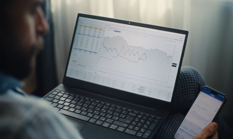 Man using a laptop and smartphone to track stock market trends and updates