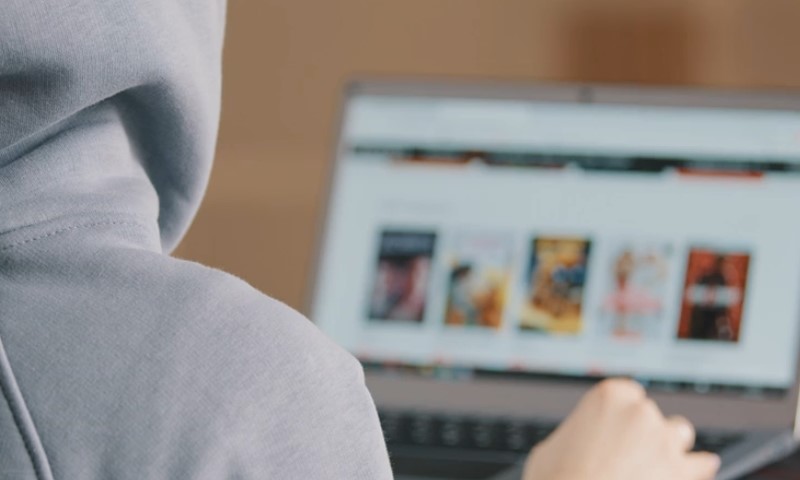 A person in a hoodie is focused on using a laptop
