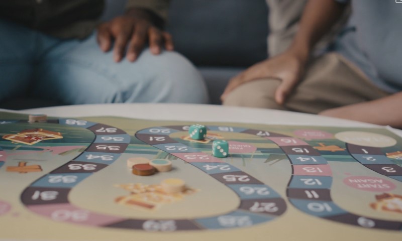 A board game is in progress on a table, with players engaged in the gameplay