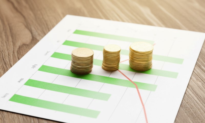 Stacks of coins are placed on a financial graph with green bars
