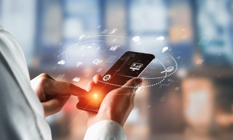 A person holds a smartphone with digital icons, like gears and graphs, hovering above it