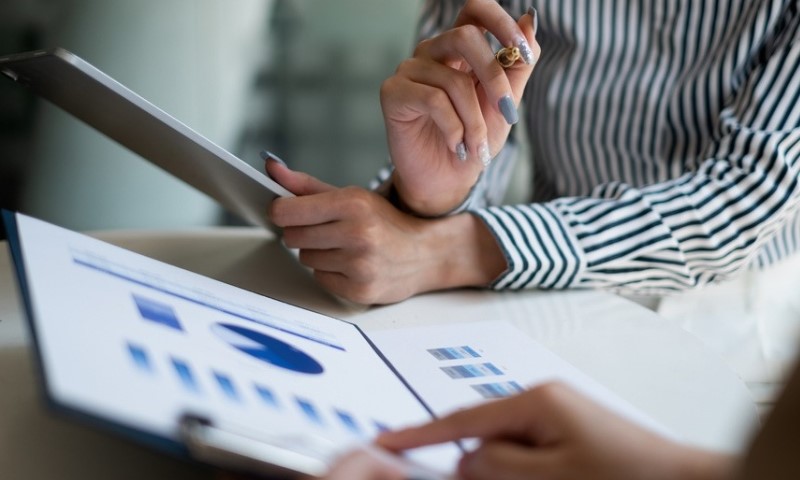 Two people review a financial report with charts on a clipboard