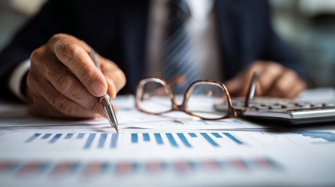 Business professional analyzing financial charts with a pen, calculator, and glasses