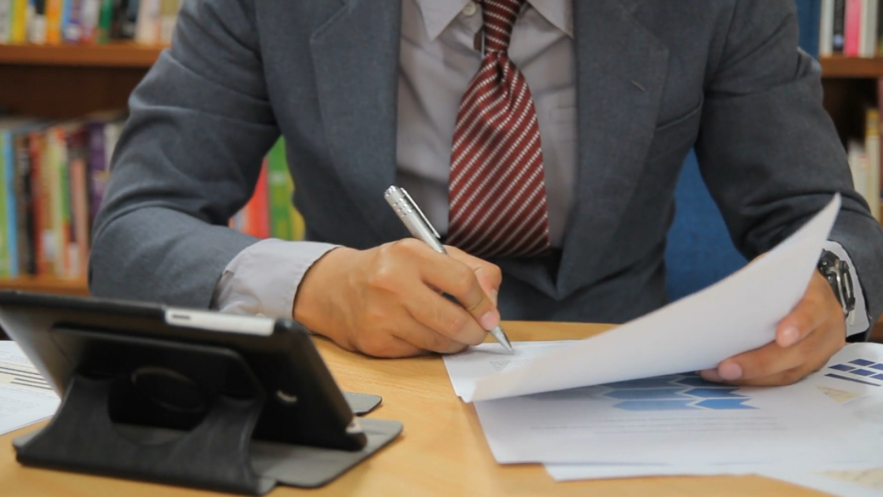 Man reviewing documents and signing paperwork at a desk with a tablet nearby